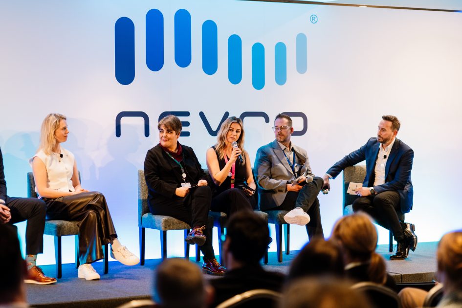 The photo of a panel discussion at a Nevro conference, featuring five professionals seated on a stage. One woman in the center is speaking into a microphone, while the others listen attentively. The backdrop displays the Nevro logo, and the audience is visible in the foreground.